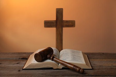 Judge's gavel, Bible and cross on wooden table against pale orange background, closeupの写真素材
