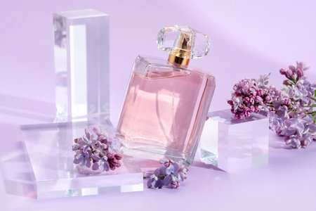 Stylish presentation of perfume bottle and lilac flowers on violet background, closeup
