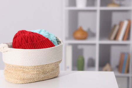 Different wool hats in wicker basket on white table indoors, space for textの写真素材