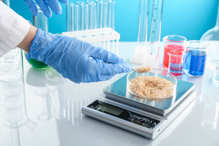 Scientist weighing Petri dish with sample on scales at white mirror table against light blue background, closeupの写真素材