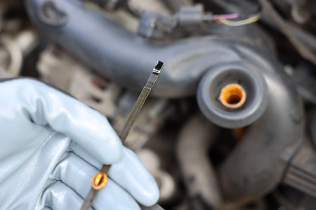 Worker checking motor oil level in car with dipstick, closeup