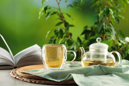 Tasty green tea with lemon in glass cup, teapot and book on white table outdoorsの写真素材