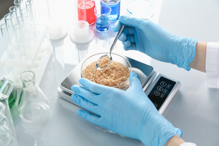 Scientist weighing Petri dish with sample on scales at white mirror table, closeupの写真素材