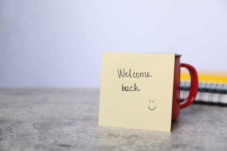 Sticky note with phrase Welcome Back and coffee on gray table, closeup. Space for textの写真素材