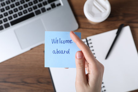 Woman holding paper note with words Welcome Aboard at wooden table, top viewの写真素材