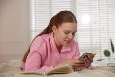 Teenage student using smartphone while studying on bed at homeの写真素材