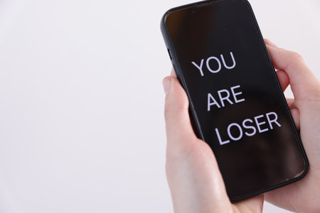 Cyber bullying. Woman holding smartphone with text You Are Loser on white background, closeup. Space for textの写真素材