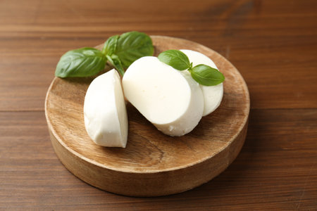 Pieces of delicious mozzarella cheese and basil leaves on wooden table, closeup