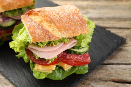 Tasty baguette sandwich with ham and vegetables on wooden table, closeupの写真素材