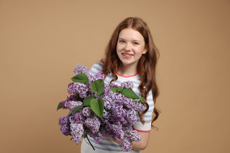 Smiling teenage girl with bouquet of lilac flowers on beige background