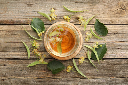 Tasty linden tea in cup, leaves and flowers on wooden table, flat layの写真素材