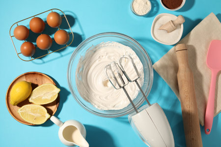 Hand mixer with whipped cream, eggs and other products on light blue table, flat layの写真素材