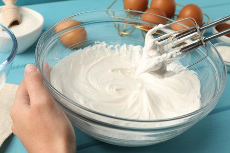 Woman whisking cream with hand mixer at light blue wooden table, closeupの写真素材
