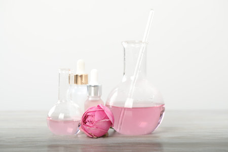Making luxury perfume. Essential oils in glassware and flowers on white wooden table, closeup