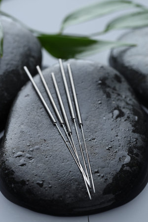 Acupuncture needles, wet spa stones and leaves on water surface, closeup