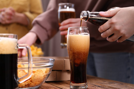 Woman pouring beer into glass at wooden table, closeup