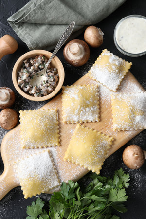Uncooked ravioli, mushrooms and sauce on black table, flat layの写真素材