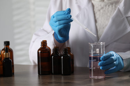 Professional perfumer developing luxury perfume at wooden table in laboratory, closeup