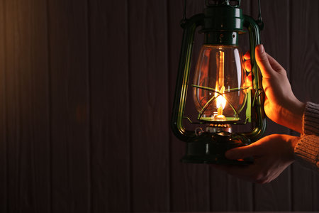 Man with vintage kerosene lamp on wooden background, closeup. Space for textの写真素材