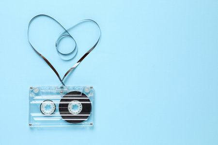 One audio cassette with heart shaped magnetic tape on light blue background, top view. Space for textの写真素材