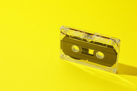 One audio cassette with magnetic tape on yellow background, closeup. Space for textの写真素材