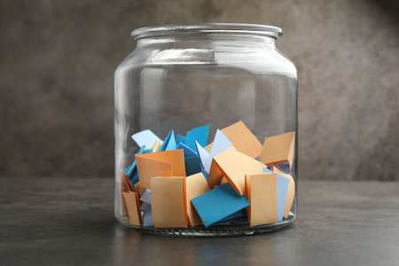 Jar with colorful pieces of paper on grey table, closeupの写真素材