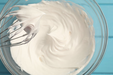 Whisk with whipped cream above bowl on table, top viewの写真素材