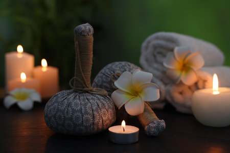 Spa composition with herbal bags, plumeria flowers and burning candles on dark table against blurred green background, closeupの写真素材