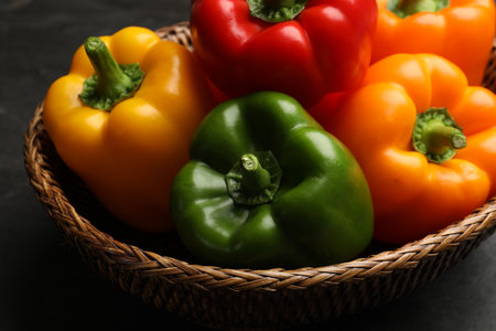 Fresh colorful bell peppers in wicker basket on dark table, closeupの写真素材