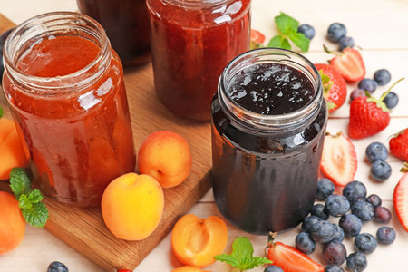 Tasty sweet jams in jars and ingredients on light wooden table, closeup