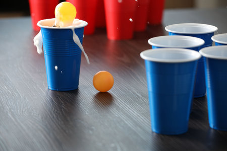 Beer pong game. Plastic cups with drinks and balls on wooden table, closeupの写真素材