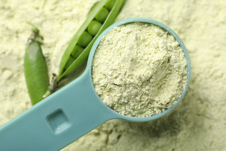 Measuring spoon and fresh pea pods on protein powder, flat layの写真素材