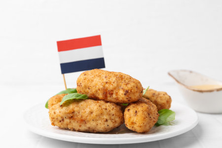 Tasty fried croquettes, basil, sauce and flag of Netherlands on white tiled table, closeupの写真素材