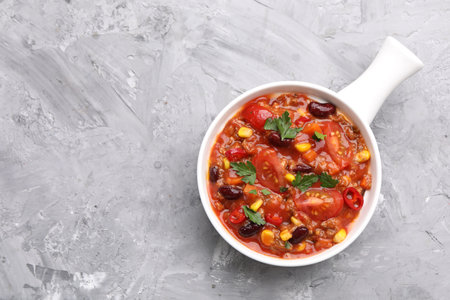 Tasty chili con carne in bowl on grey textured table, top view. Space for textの写真素材