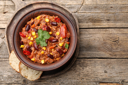 Tasty chili con carne in bowl and bread slices on wooden table, top view. Space for textの写真素材