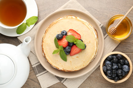 Delicious crepes with berries, cream, mint, honey and tea on wooden table, flat layの写真素材