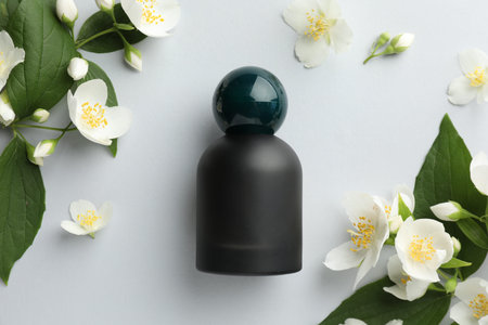 Bottle of perfume and jasmine flowers on light background, flat lay