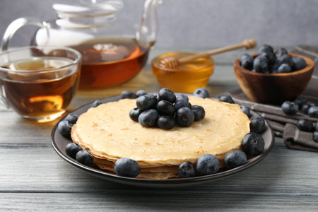 Delicious crepes with blueberries, honey and tea on grey wooden table, closeupの写真素材