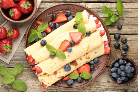 Tasty crepes with berries, cream and mint on wooden table, flat layの写真素材