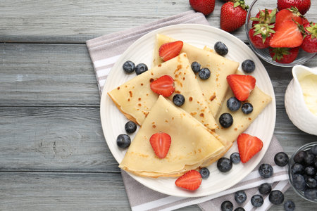 Delicious crepes with berries and cream on grey wooden table, flat lay. Space for textの写真素材