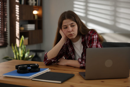 Stressed teenage girl studying at desk indoors