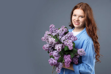 Smiling teenage girl with bouquet of lilac flowers on grey background. Space for textの写真素材