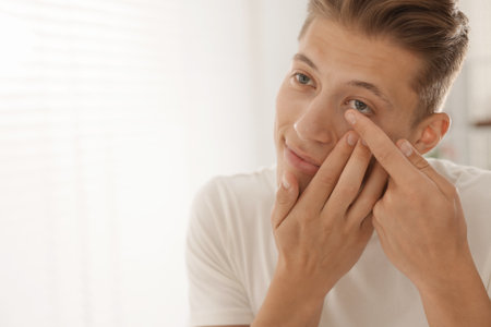 Man putting in contact lens at home. Space for textの写真素材
