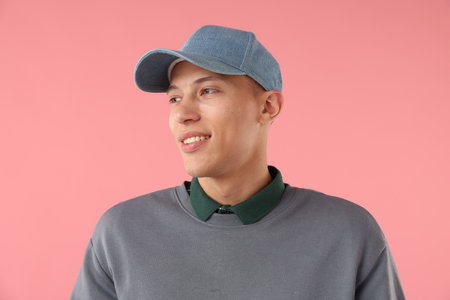 Young man in stylish baseball hat on pink backgroundの写真素材