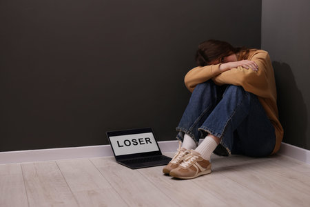 Upset teenage girl and laptop with text on floor indoors. Space for text