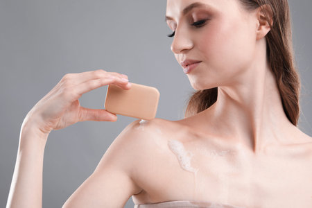 Beautiful woman with soap bar on grey background, closeup