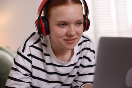 Teenage student in headphones using laptop while studying at home