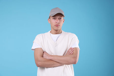 Young man wearing stylish grey baseball hat on light blue background