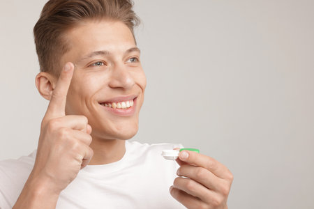 Man with contact lens and case on light background. Space for textの写真素材