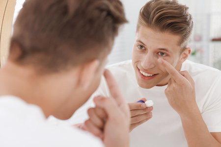 Man putting in contact lens near mirror at homeの写真素材